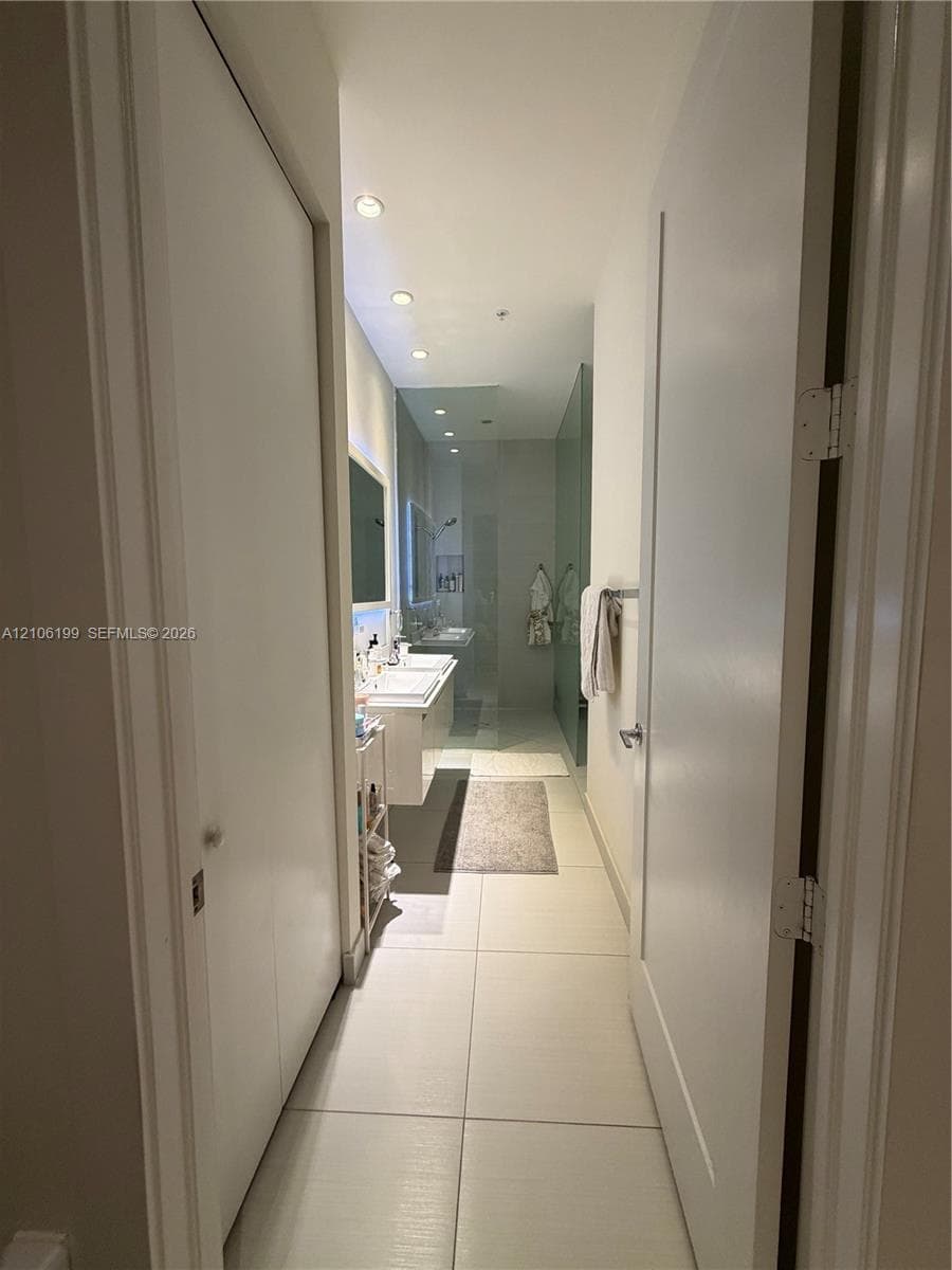 Bathroom featuring large-format floor tile, floating dual-sink vanity, recessed ceiling lighting, and a glass-enclosed shower