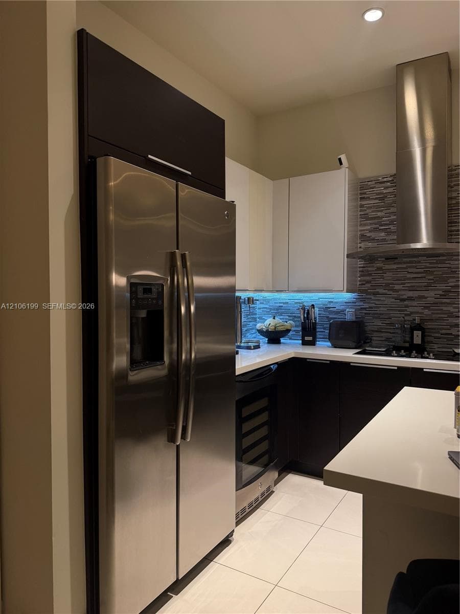 Kitchen featuring dual-tone cabinetry, stainless steel appliances, a built-in wine refrigerator, a patterned stone-look backsplash, and a stone-surface island countertop