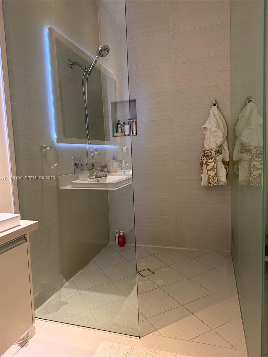 Walk-in shower featuring a frameless glass enclosure, neutral tile surround, built-in wall niche, overhead shower head, and tiled flooring