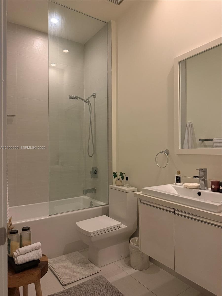 Full-height glass shower panel, integrated bathtub, vanity with rectangular basin, wall-mounted mirror, and tile flooring