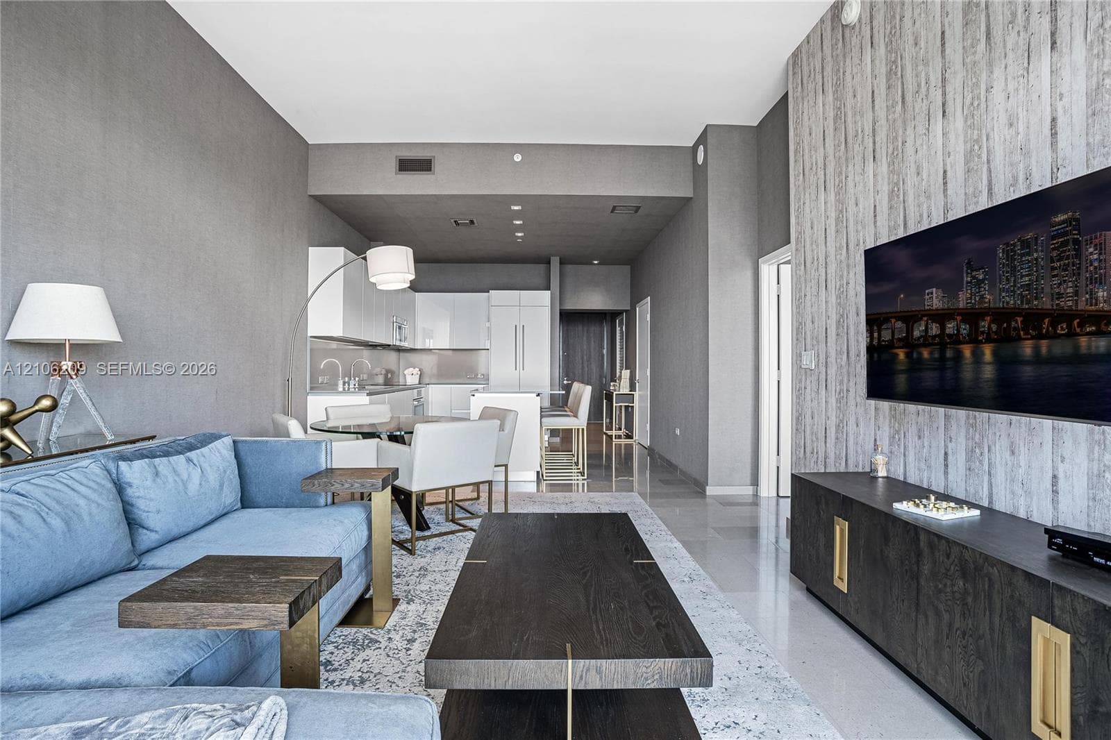 Open-concept living space featuring high ceilings, textured accent wall, sleek white kitchen cabinetry, and polished flooring