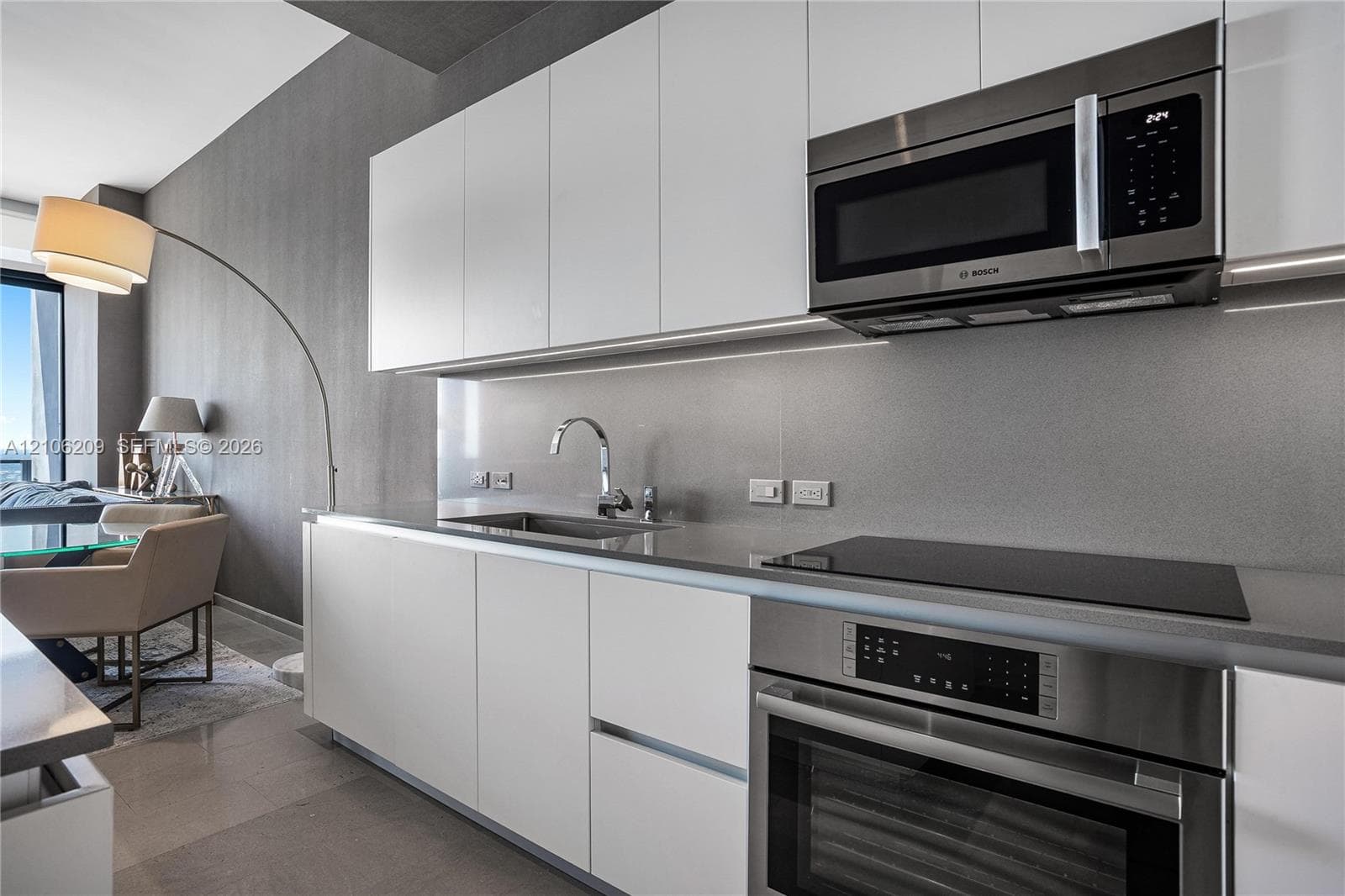 Modern kitchen featuring white flat-panel cabinetry, stainless steel appliances, a sleek induction cooktop, and a monochromatic backsplash