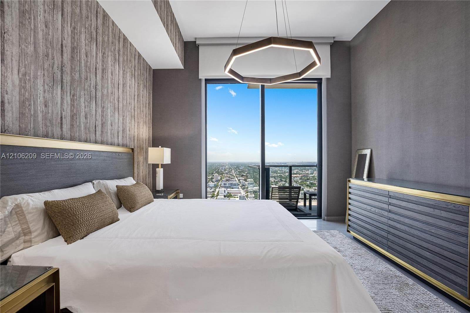 Floor-to-ceiling glass sliding door, geometric LED pendant lighting, textured wall detailing, and a balcony with an expansive urban backdrop