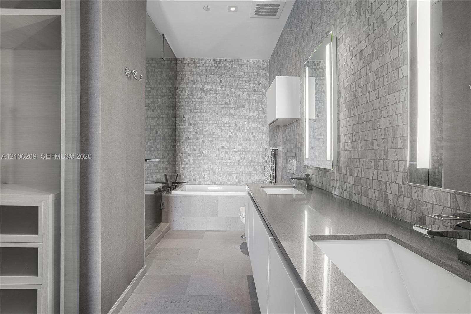 Dual-sink vanity with quartz countertop, wall-mounted backlit mirrors, soaking tub, glass-enclosed shower, and stone tile wall cladding