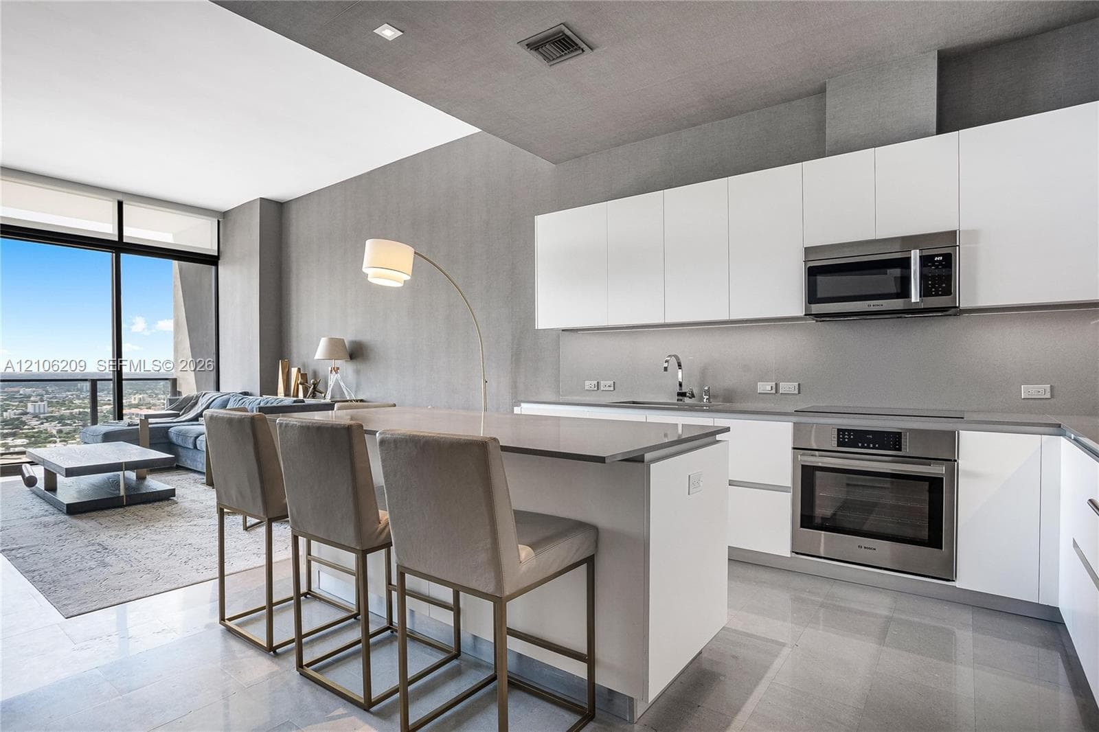Modern kitchen featuring white flat-panel cabinetry, a central island with a solid-surface countertop, stainless steel appliances, and tile flooring