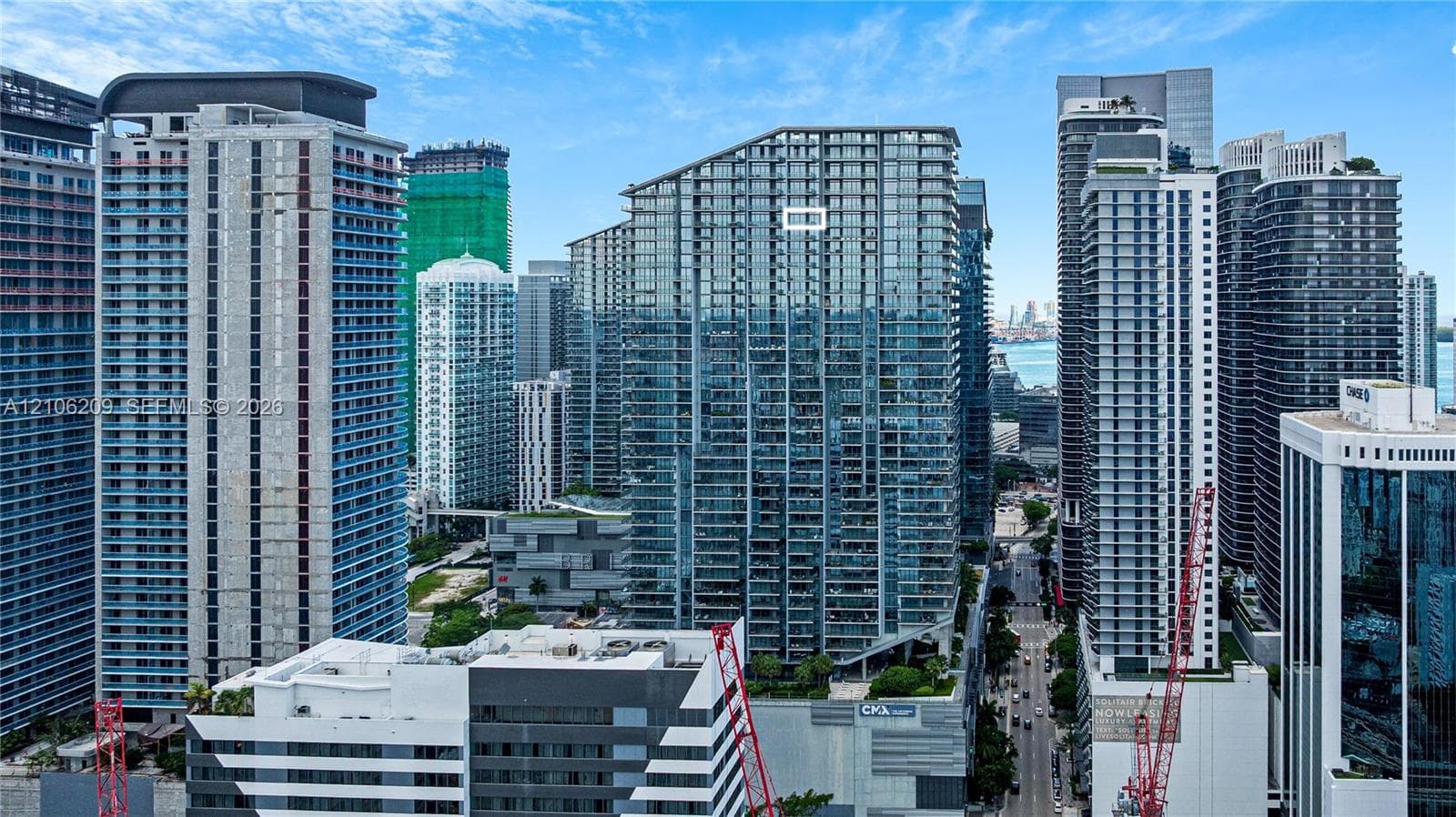 High-rise residential tower featuring a glass-curtain facade, stacked balcony design, and a prominent angular roofline within an urban metropolitan corridor