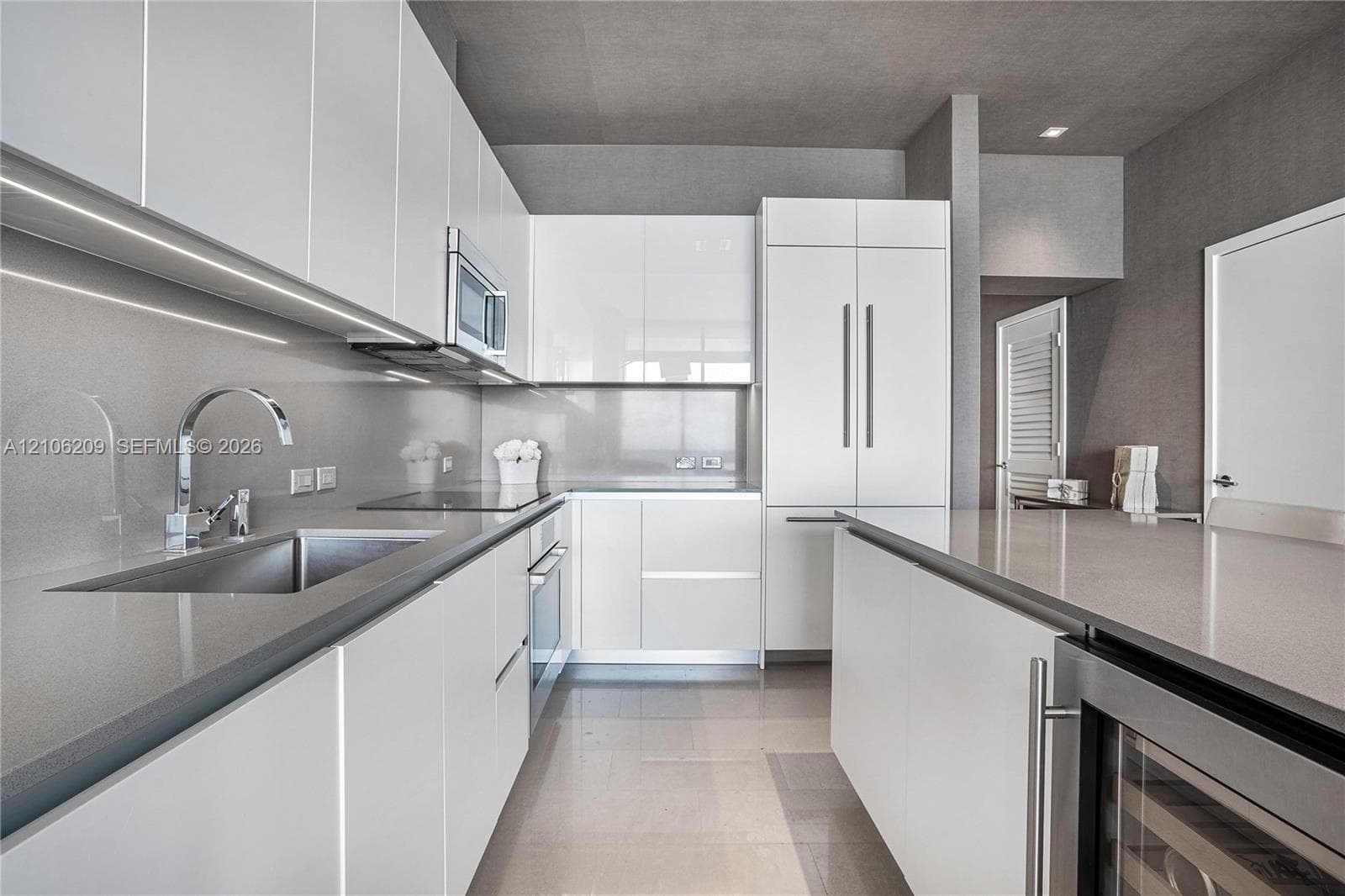 Modern kitchen featuring flat-panel white cabinetry, solid-surface countertops, integrated stainless steel appliances, and a built-in wine refrigerator