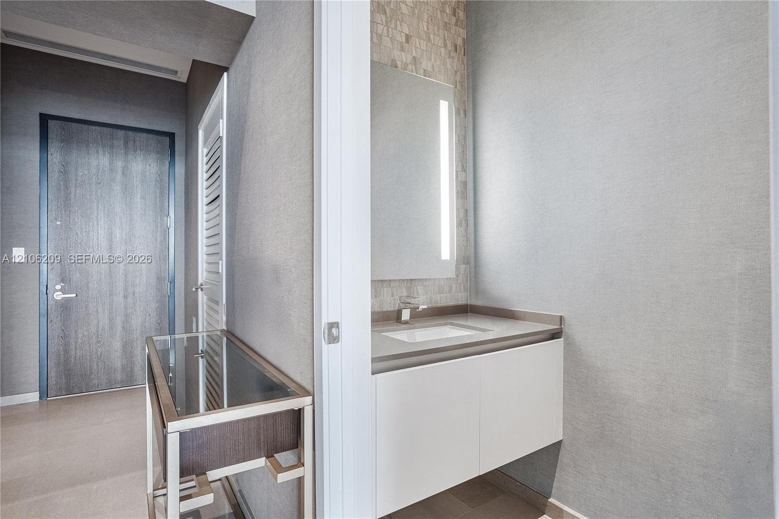 Floating white vanity with solid-surface countertop and integrated sink, vertical LED-lit mirror, and mosaic tile backsplash