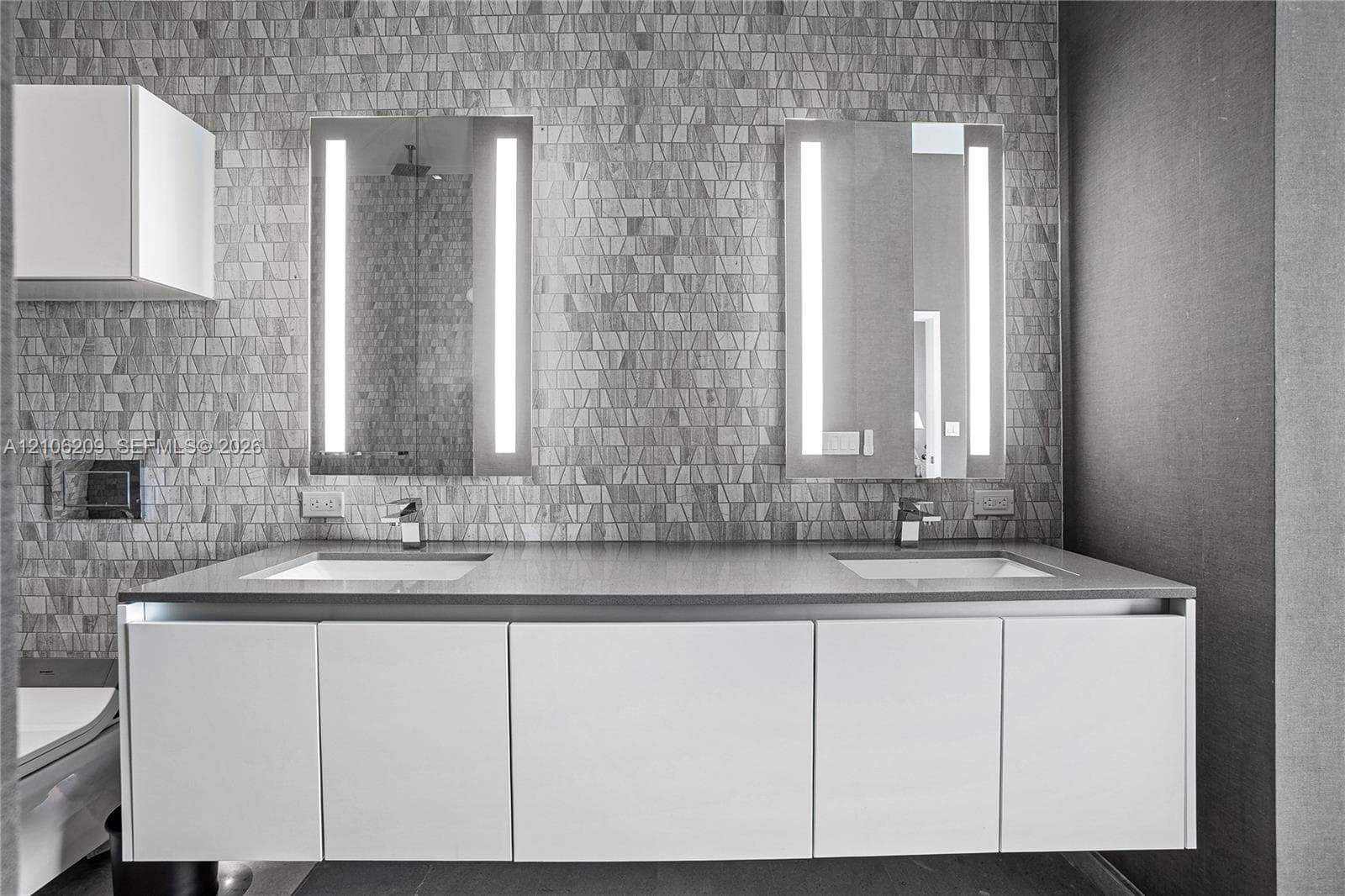 Floating white vanity with dual under-mount sinks, solid-surface countertop, rectangular LED-lighted mirrors, and geometric stone tile backsplash