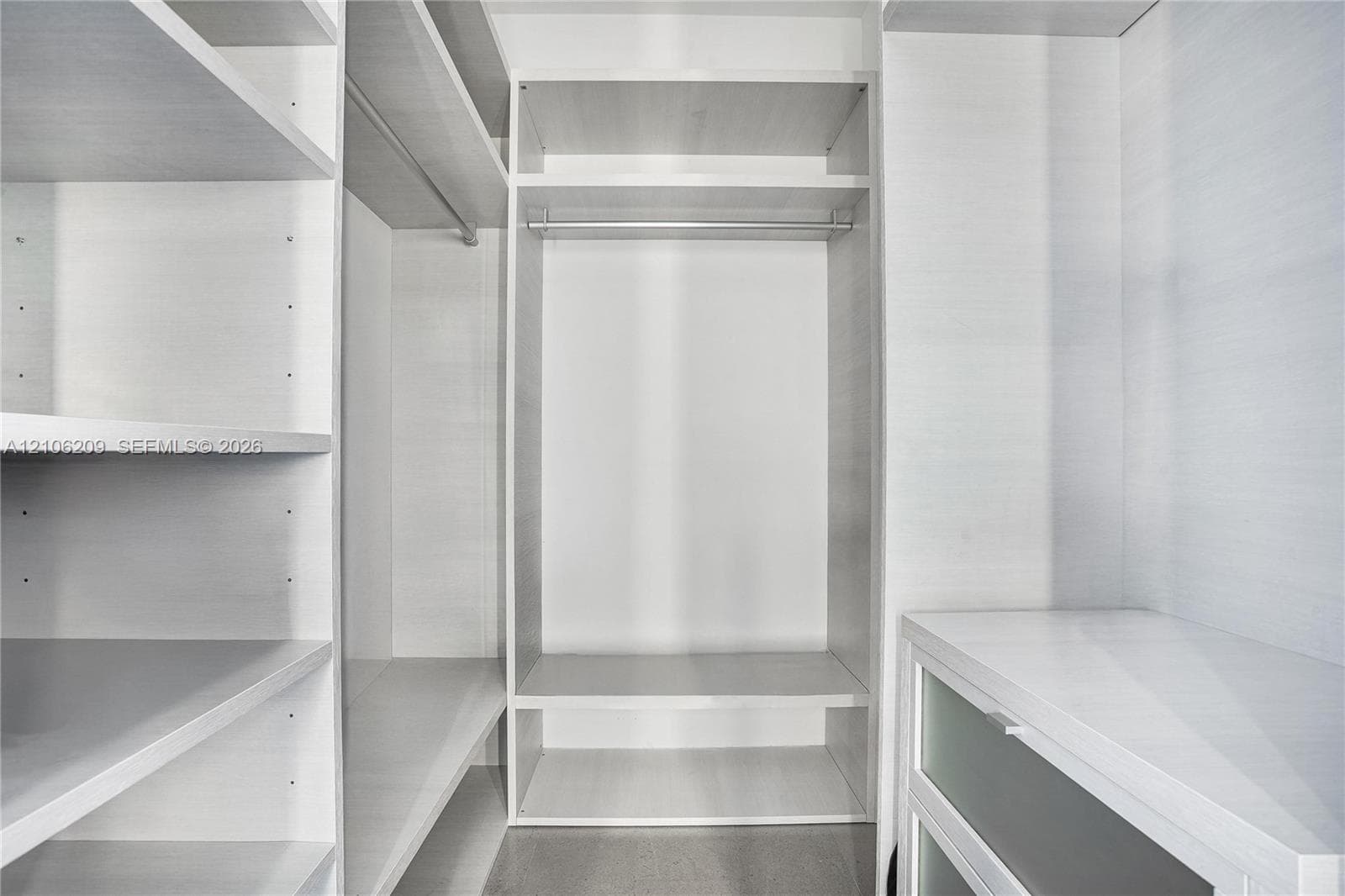 Custom reach-in closet featuring white wood-finish shelving, multiple hanging rods, and built-in cabinetry with frosted glass-panel drawers