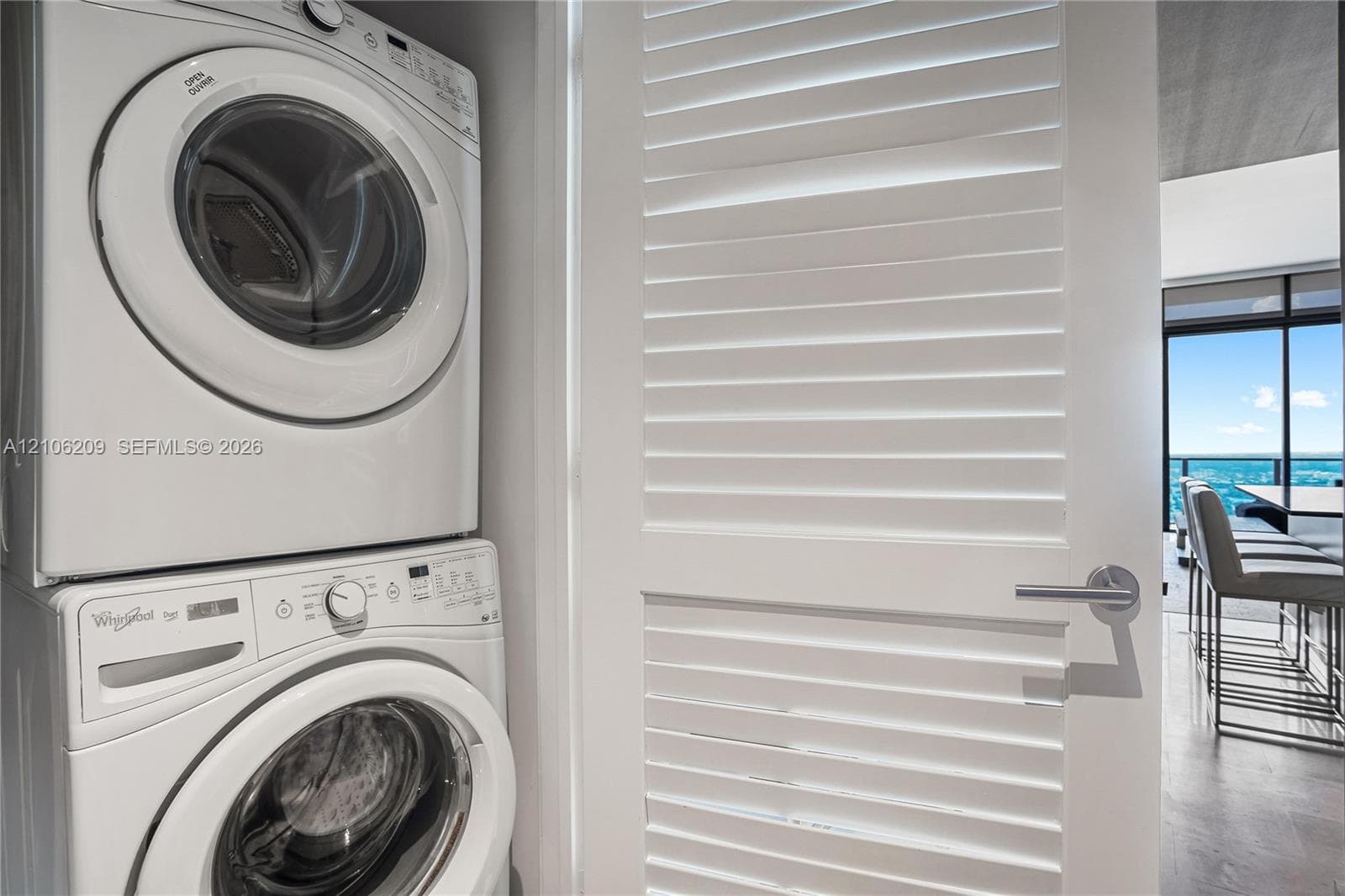 Stacked front-loading laundry unit paired with a white louvered door featuring a cylindrical brushed metal handle
