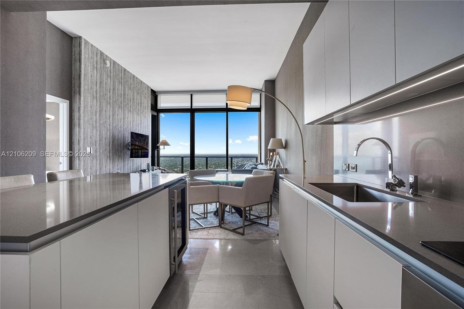 Kitchen featuring flat-panel cabinetry, quartz countertops, integrated wine refrigeration, under-cabinet lighting, and stainless steel sink hardware