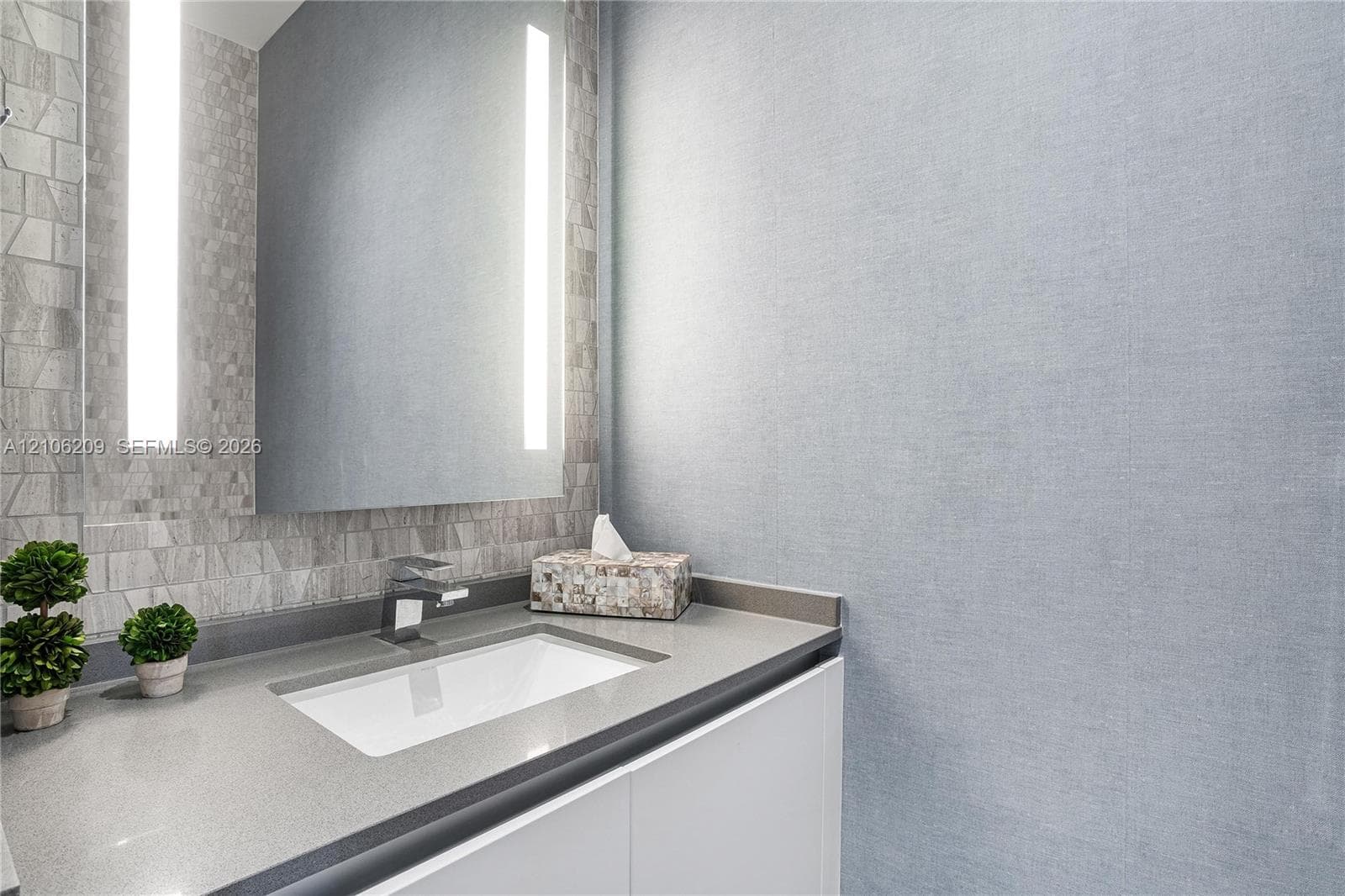 Modern vanity featuring a solid-surface countertop, rectangular undermount sink, integrated vertical lighting, and textured tile backsplash