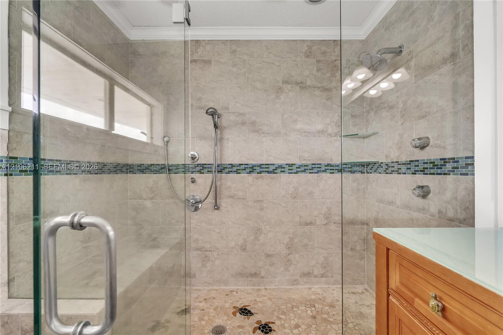 Walk-in shower featuring glass paneling, floor-to-ceiling tile with a decorative mosaic accent band, a built-in tiled bench, stone pebble flooring with inlaid tile motifs, and a multi-function shower system