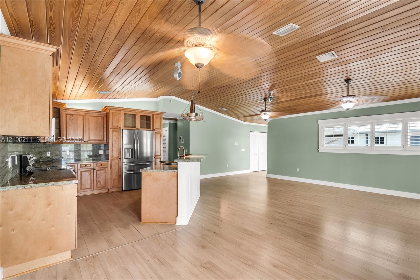 Vaulted wood-plank ceiling, natural wood-finish cabinetry, stone countertops, wood-finish flooring, and multiple ceiling fans