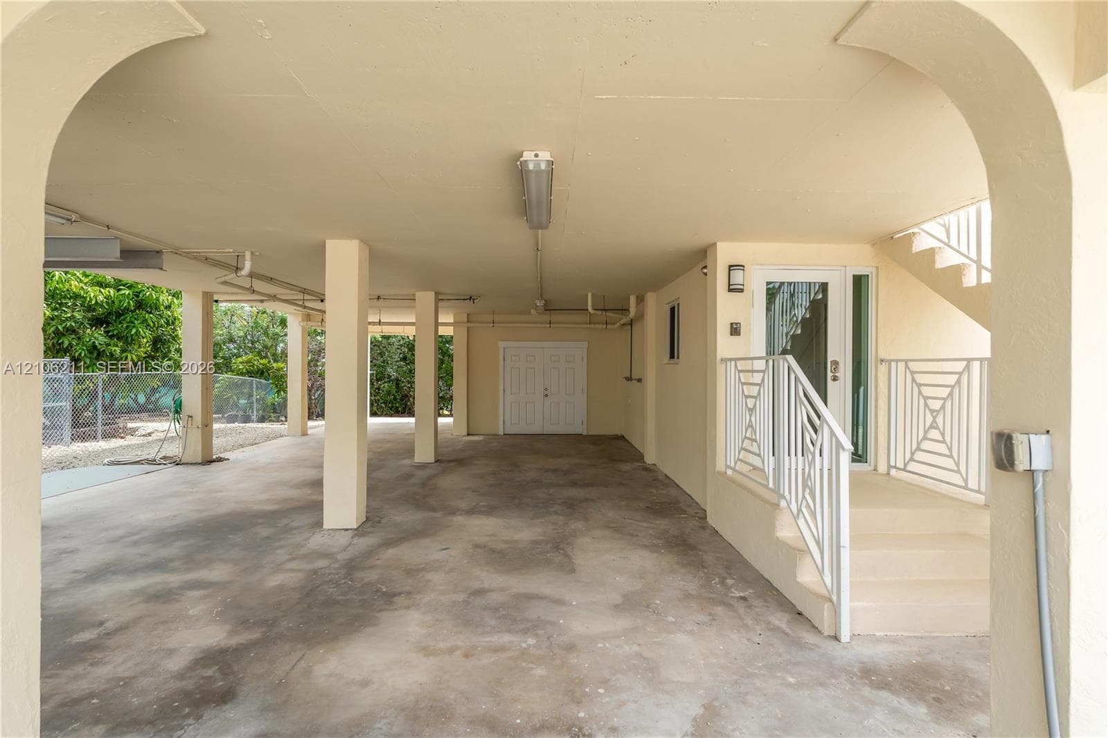 Covered carport with architectural archways, concrete flooring, dual-door utility entrance, and staircase with metal railings