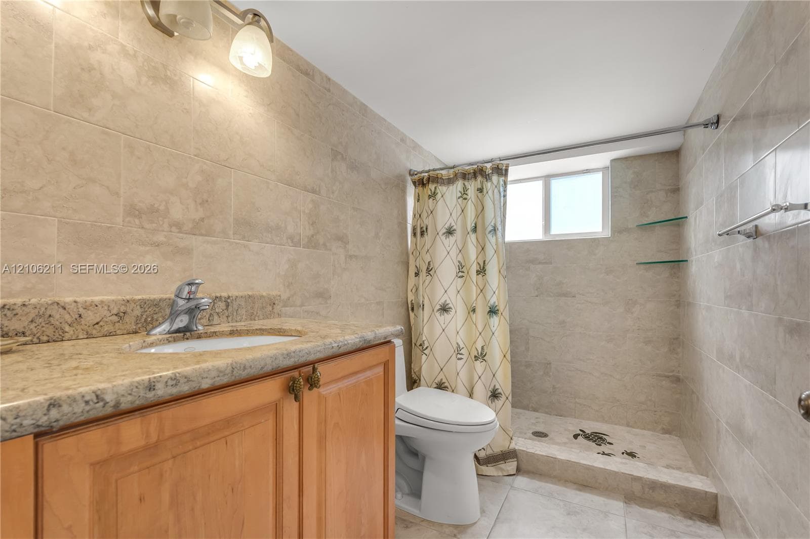 Bathroom featuring a stone-topped vanity with an undermount sink, natural stone wall tiling, a walk-in shower with floating glass shelving, and dual-light wall sconce