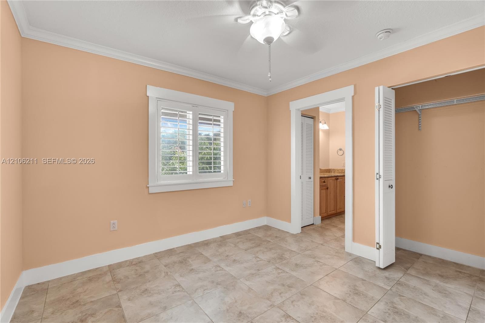 Neutral-toned room featuring ceramic tile flooring, crown molding, plantation shutters, a ceiling fan with integrated lighting, and a closet with bifold louvered doors