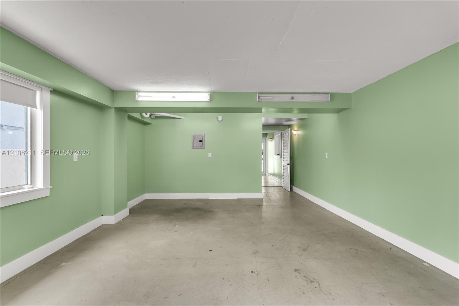 Multi-purpose interior space featuring smooth concrete flooring, overhead fluorescent lighting, and a single-pane window