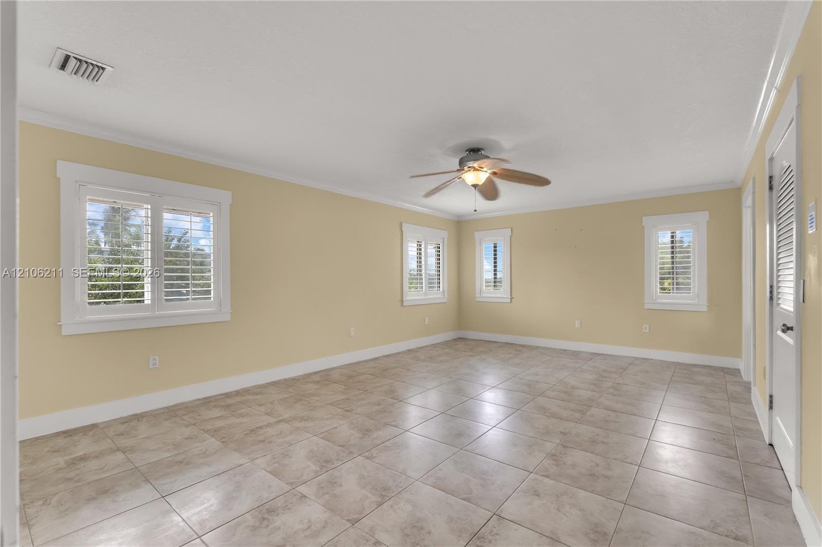 Neutral-toned interior room featuring large-format ceramic tile flooring, plantation shutters, and a ceiling fan with integrated lighting