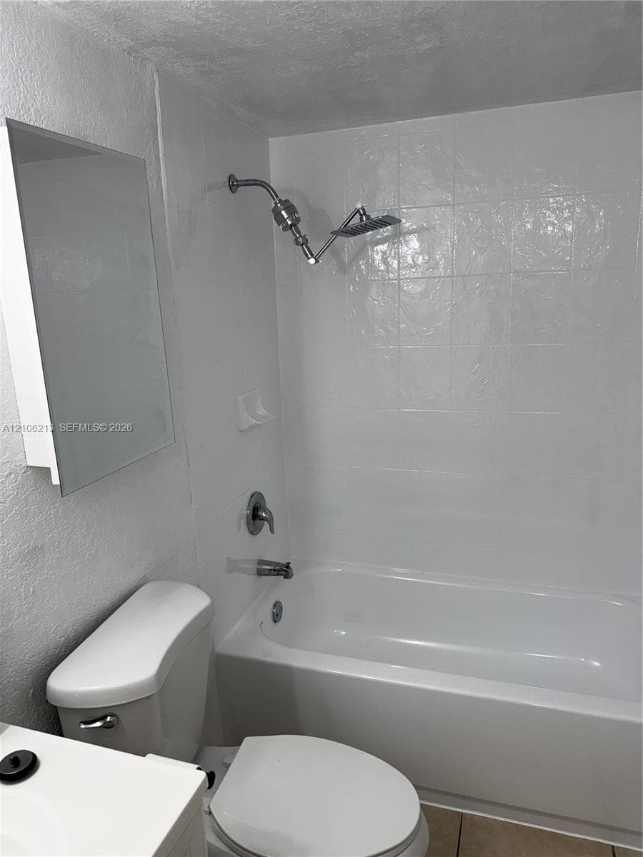 Full bathroom featuring a white porcelain tub with integrated tile surround, wall-mounted shower head, recessed soap dish, and mirrored medicine cabinet
