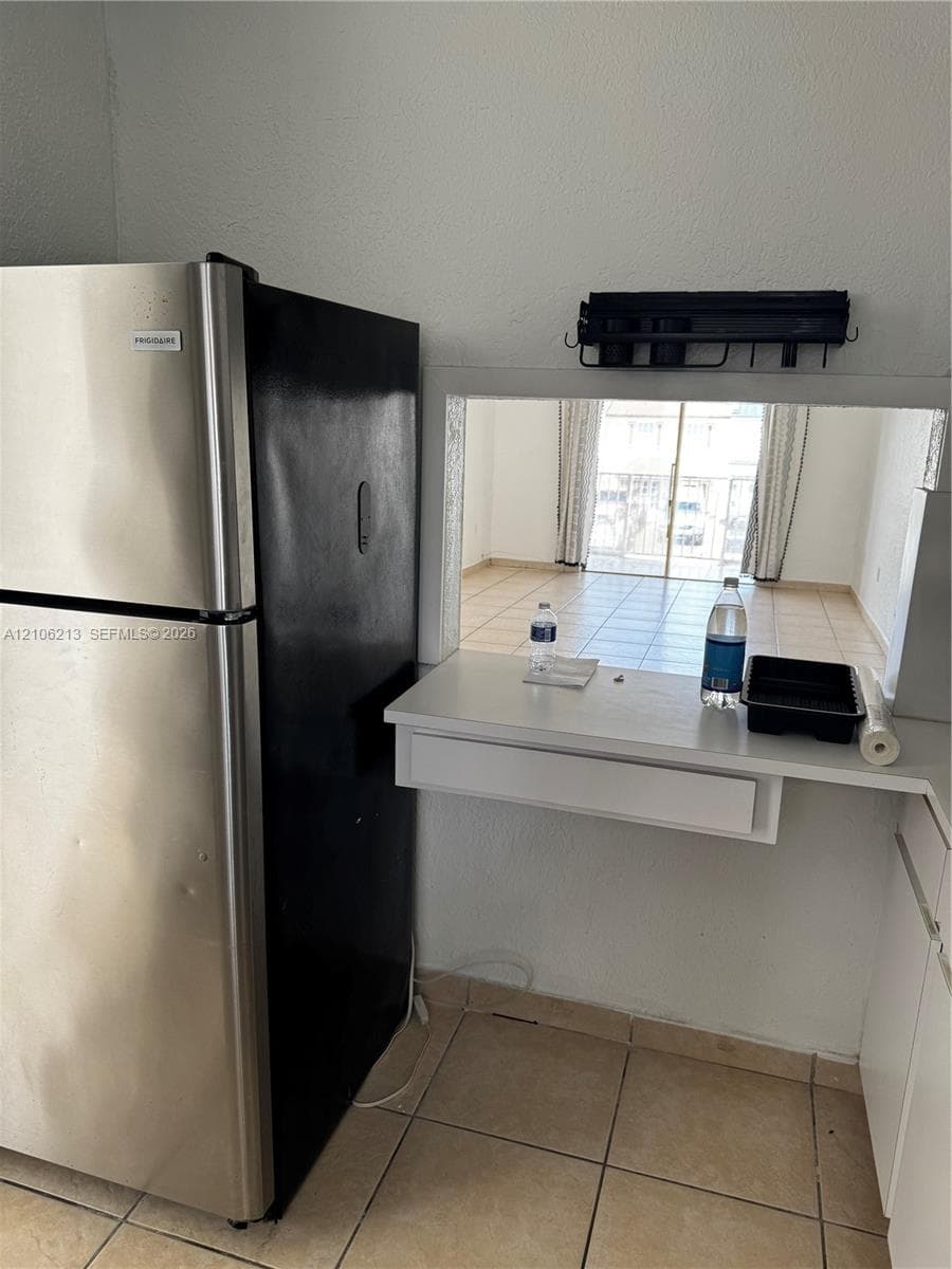 Stainless steel refrigerator with a black finish, ceramic tile flooring, and a built-in pass-through service counter featuring a storage drawer