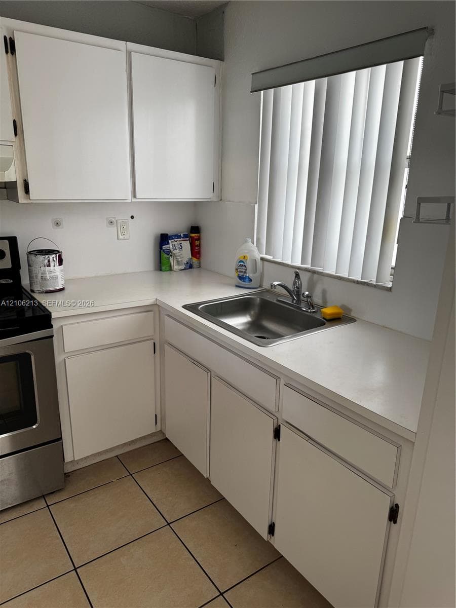 Kitchen featuring white cabinetry, solid-surface countertops, stainless steel sink with metal faucet, and tile flooring
