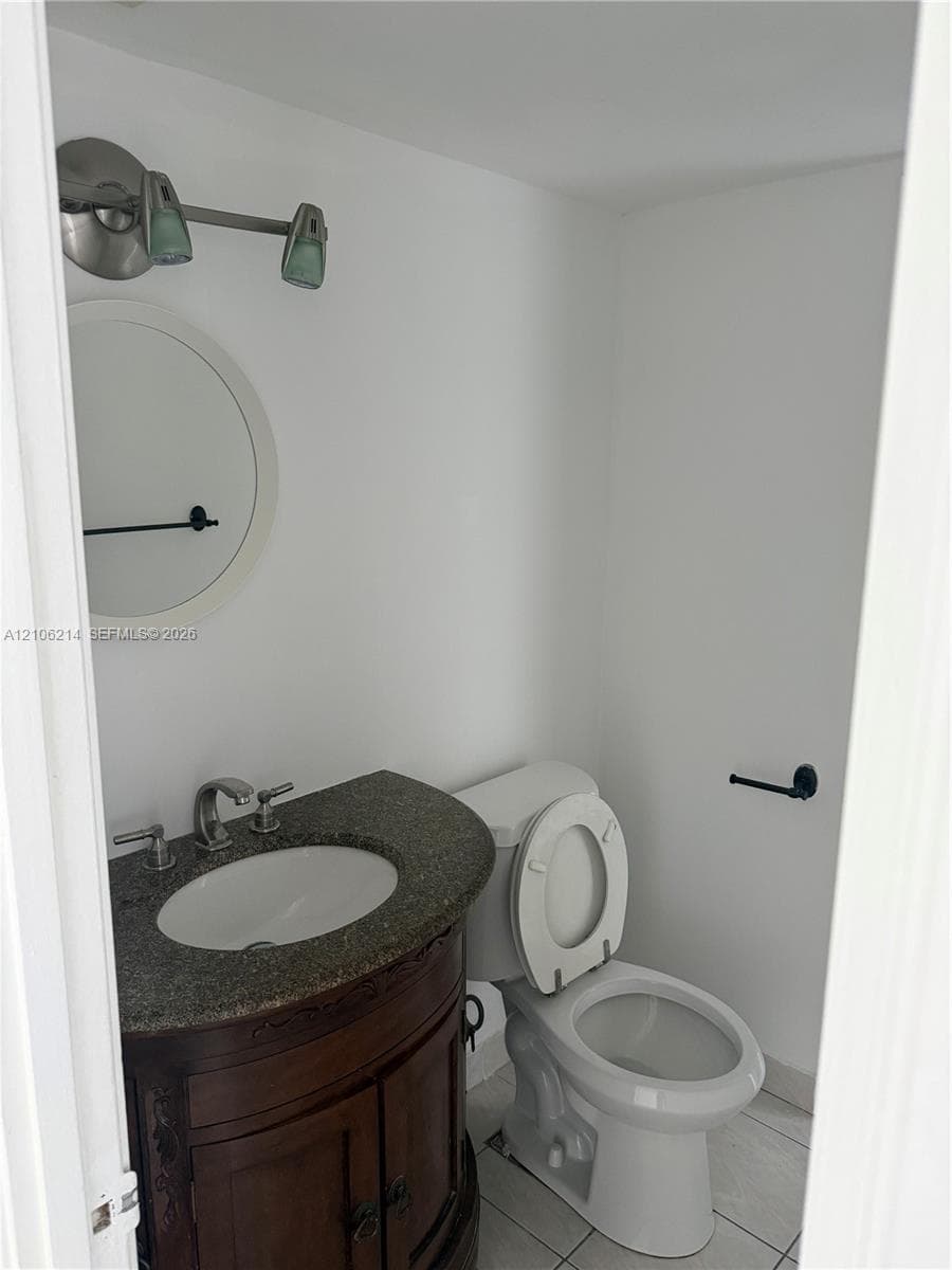 Dark wood vanity with a stone countertop, oval undermount sink, circular wall mirror, two-light fixture, and ceramic tile flooring