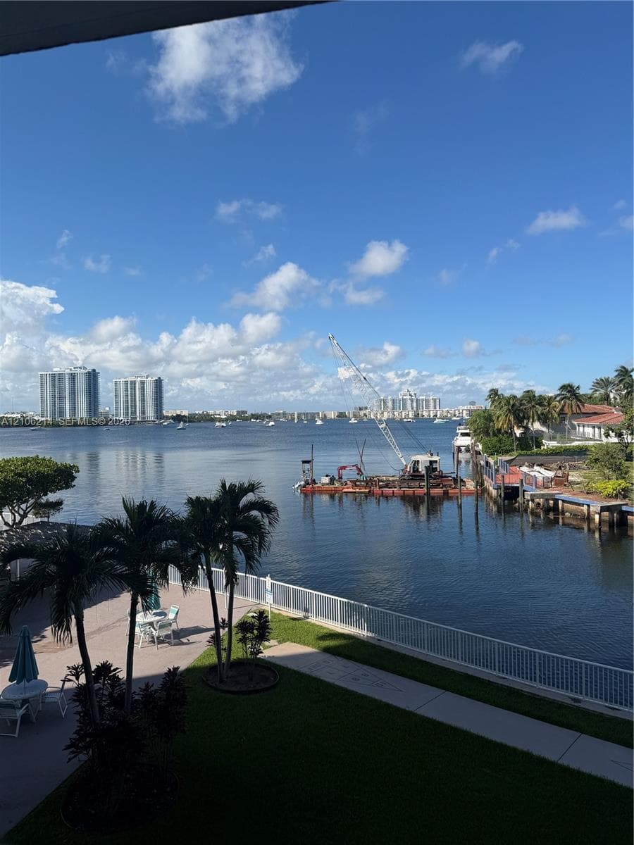 Waterfront property featuring a paved patio, perimeter fencing, and mature palm trees