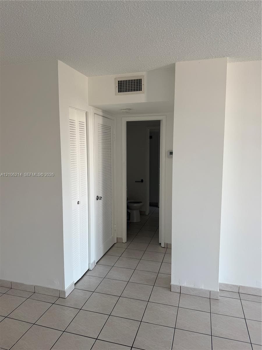 Interior space featuring neutral tile flooring and two sets of louvered-style closet doors