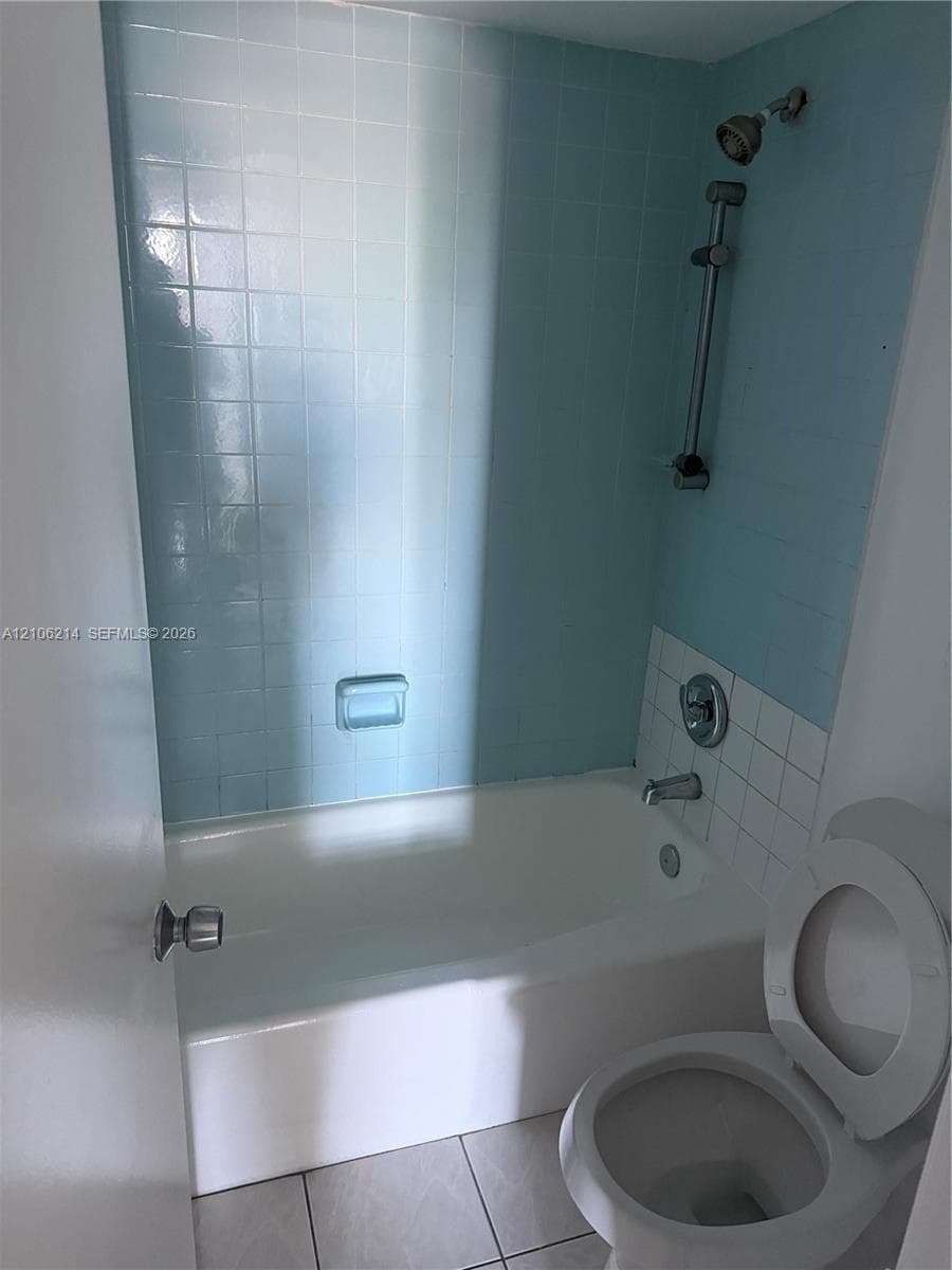 Full bathroom featuring a tub-shower combination with light blue tile surround, adjustable shower head on a sliding bar, and tile flooring
