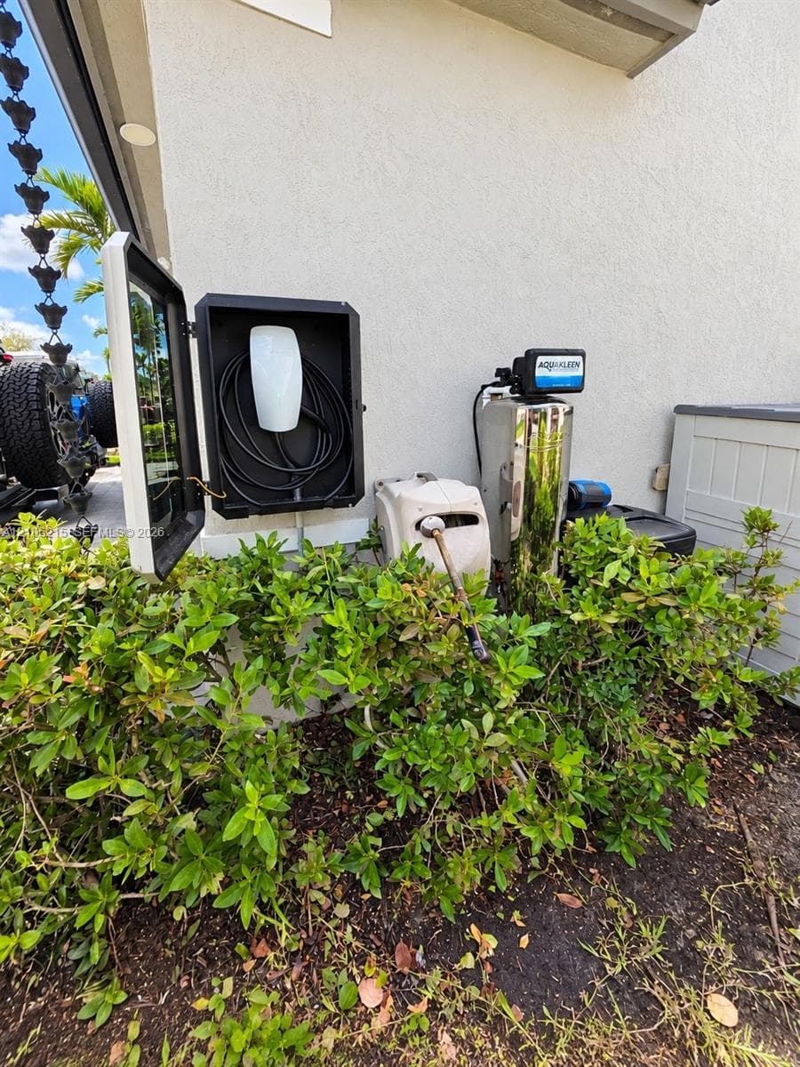 Exterior charging station featuring a wall-mounted electric vehicle charger enclosed in a protective housing, accompanied by a whole-home water filtration system