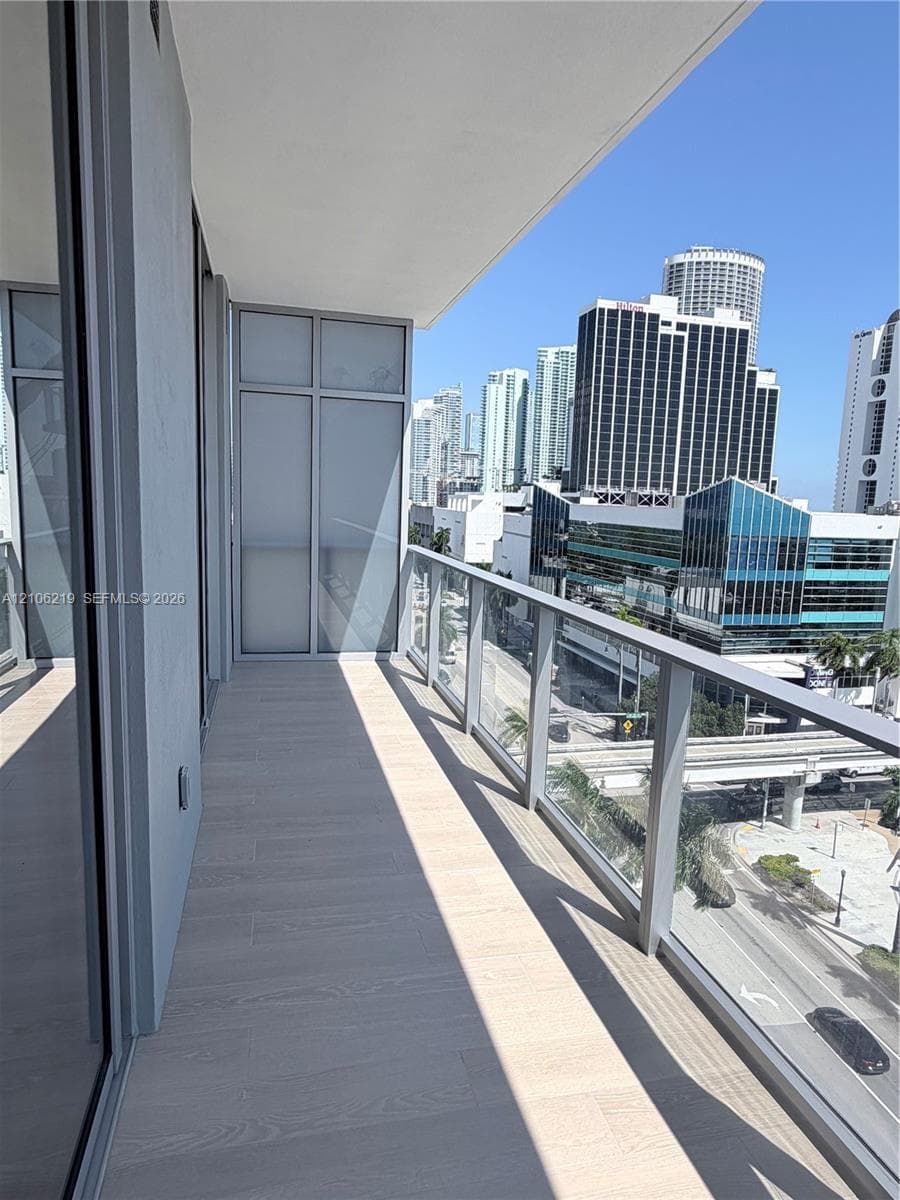 Covered balcony featuring wood-finish flooring, glass panel railings, and full-height glass exterior doors