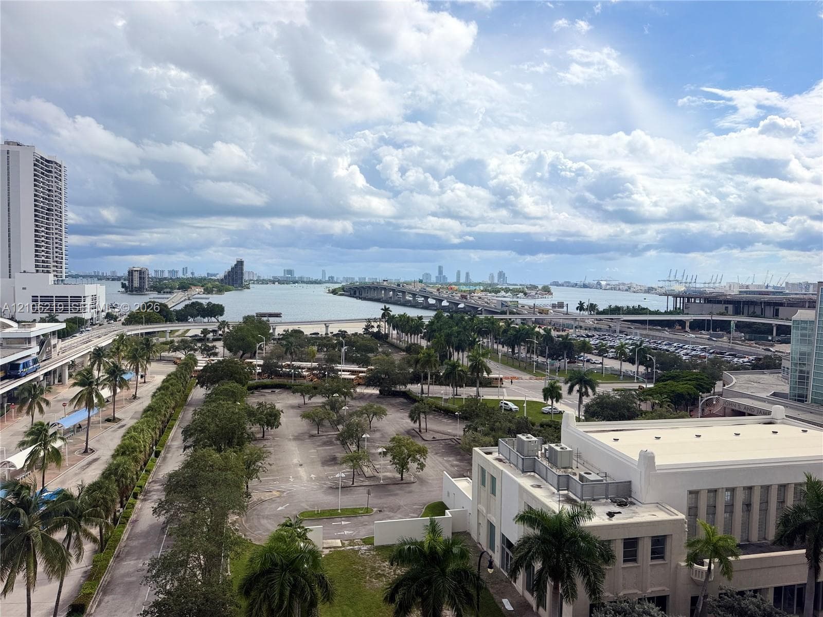 Panoramic water and city skyline outlook featuring a concrete bridge, maritime waterway, urban thoroughfares, and mature palm trees