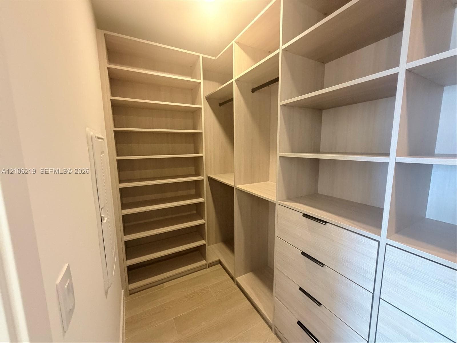 Walk-in closet featuring light wood-finish shelving, custom built-in cabinetry with drawers, dark hardware, and wood-finish tile flooring