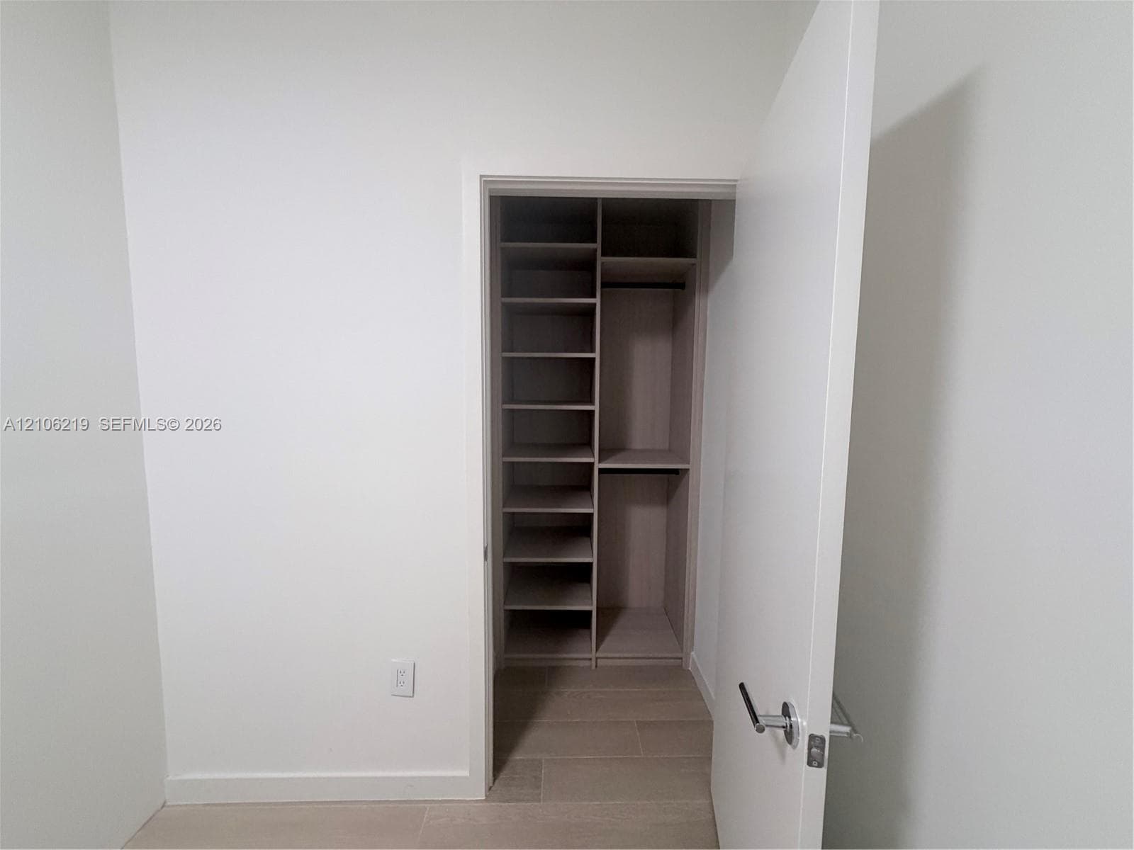 Storage area featuring custom wood-finish built-in shelving, multiple open storage compartments, and a hanging rod, finished with neutral-tone flooring