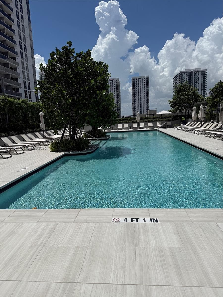 Swimming pool with tiled decking, integrated landscaping, and surrounding urban high-rise structures