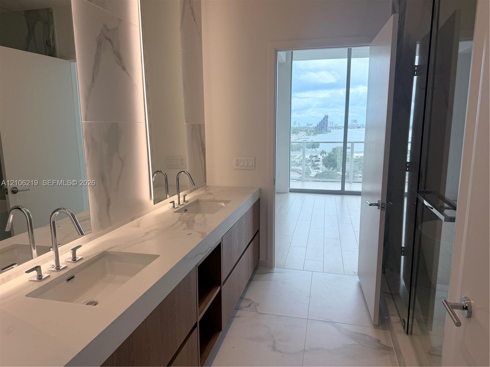 Double vanity with integrated sinks, stone-finish countertops, wood-finish cabinetry, floor-to-ceiling tiled backsplash, and glass-enclosed shower