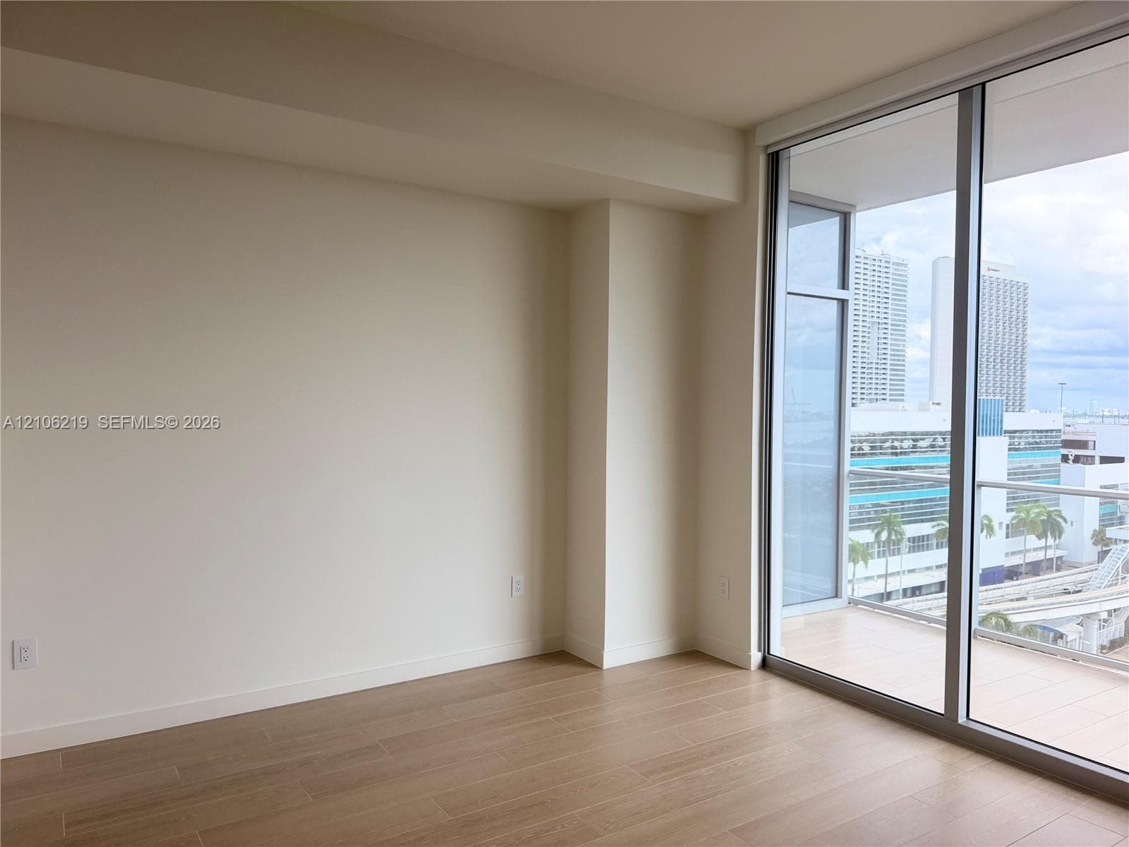 Floor-to-ceiling glass sliding doors, wood-finish flooring, and a private balcony with metallic railing