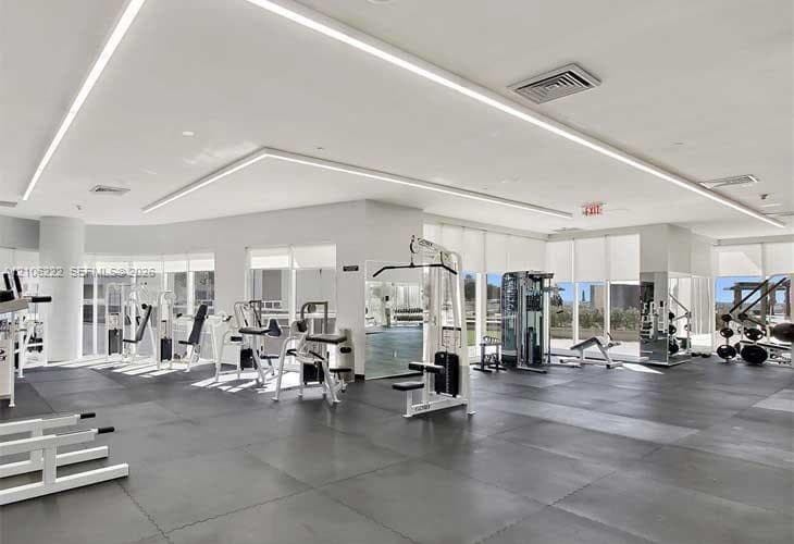Fitness center featuring resilient rubber flooring, recessed architectural LED lighting, expansive floor-to-ceiling windows, and mirrored wall surfaces