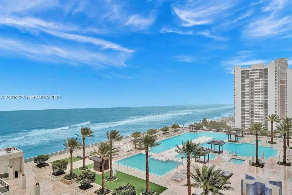 Oceanfront terrace featuring multiple swimming pools, stone-paved decking, built-in pergolas, and established palm trees