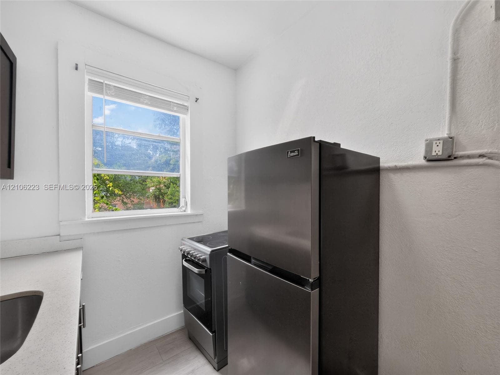 Stainless steel refrigerator and freestanding range, neutral solid-surface countertop, and window with natural illumination