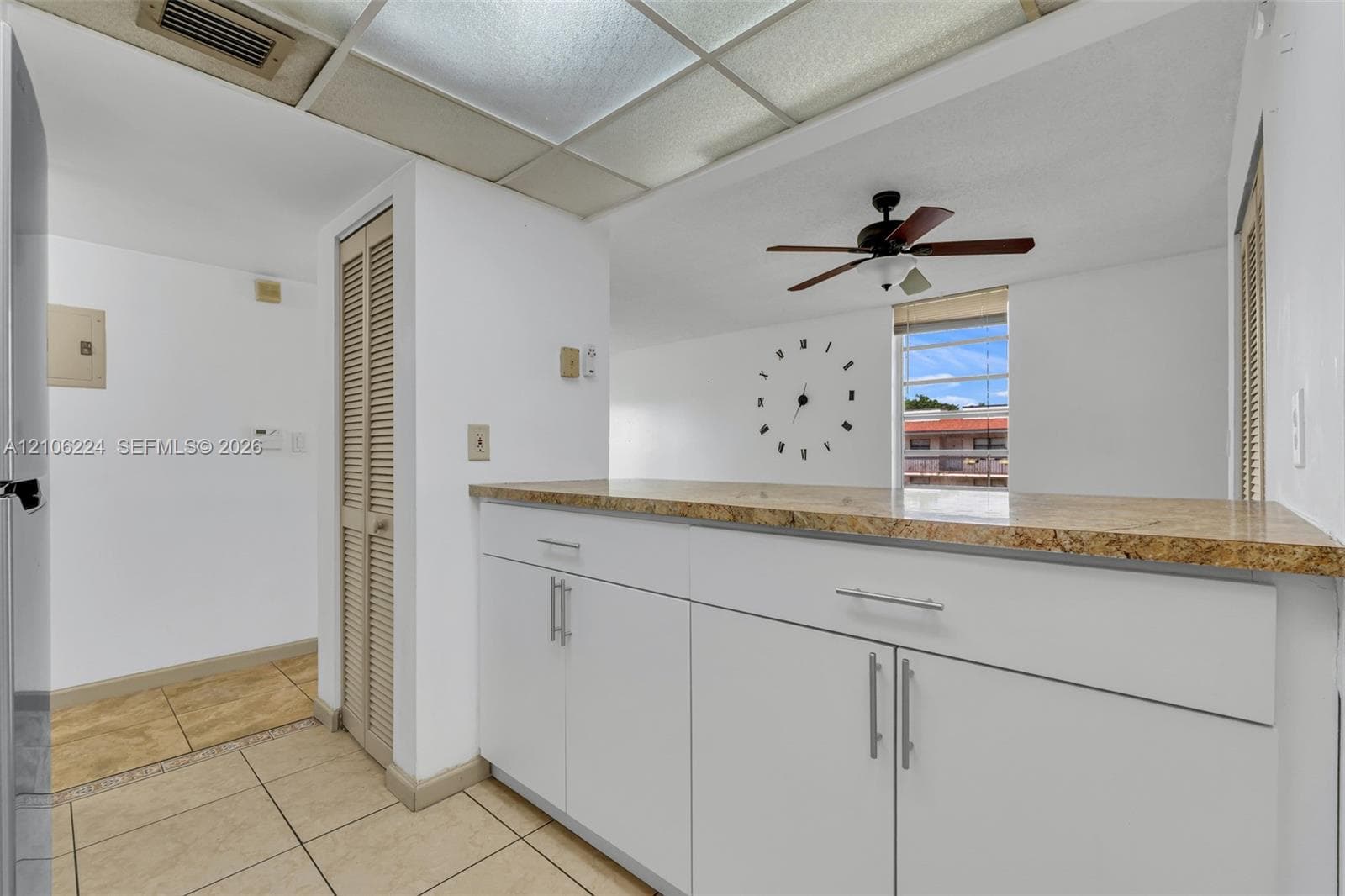 Kitchen area featuring white cabinetry, stone-finish countertops, tile flooring, and a ceiling-mounted fan