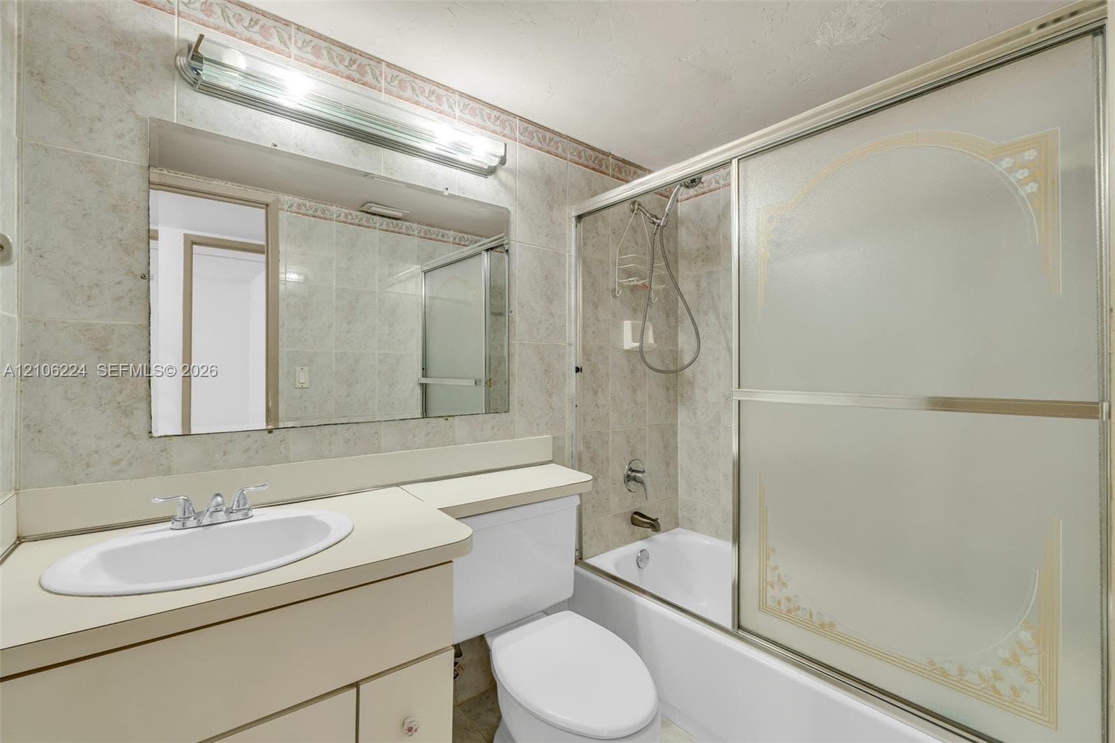 Bathroom featuring a built-in vanity with a stone-surface countertop, an oval drop-in sink, a wall-mounted full-width mirror with overhead light fixture, and a shower-tub combination enclosed by sliding frosted glass doors