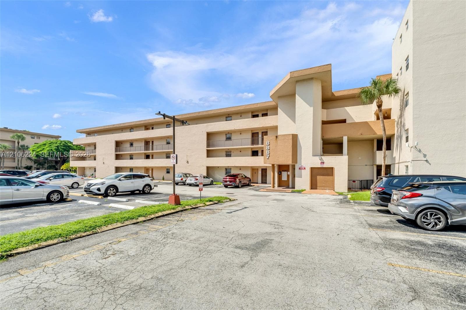 Multi-story residential building exterior featuring stucco cladding, recessed private balconies, ground-level parking, and architectural roofline accents
