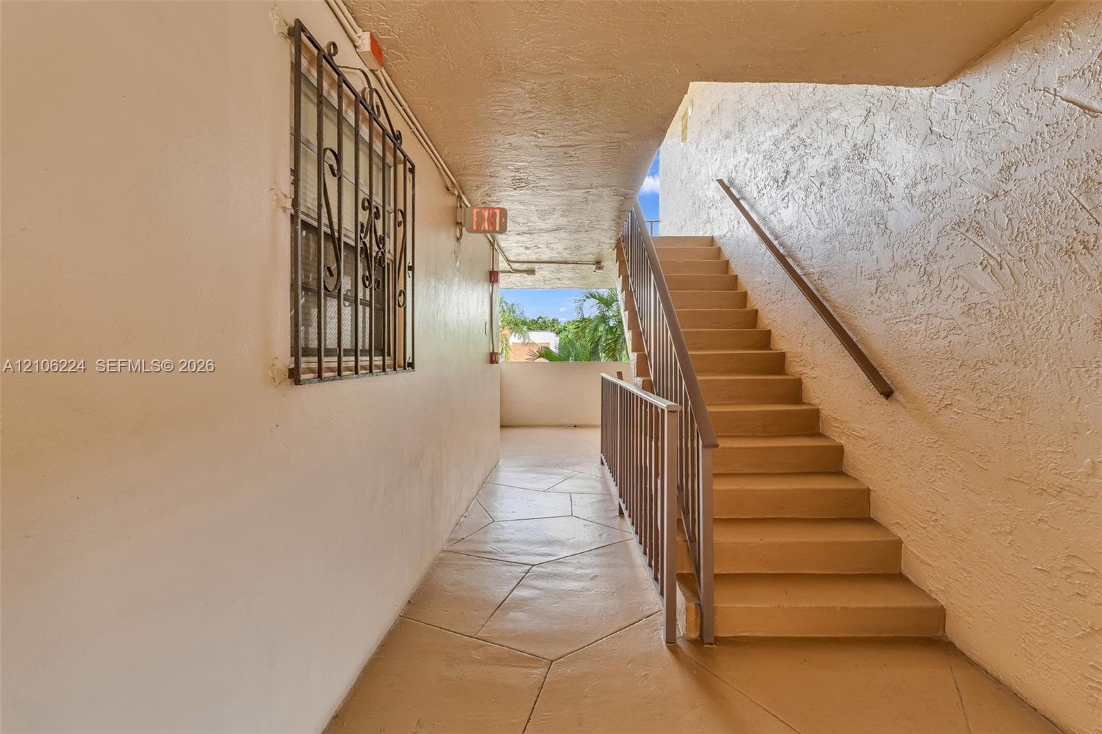 Exterior staircase featuring concrete steps, metal handrailing, stone-patterned tile flooring, and a decorative metal window grate
