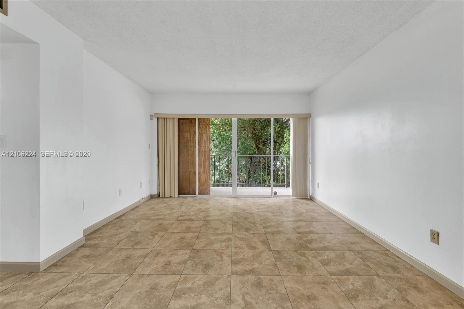 Interior space featuring large-format ceramic tile flooring, neutral wall finishes, and floor-to-ceiling glass sliding doors opening to an exterior balcony