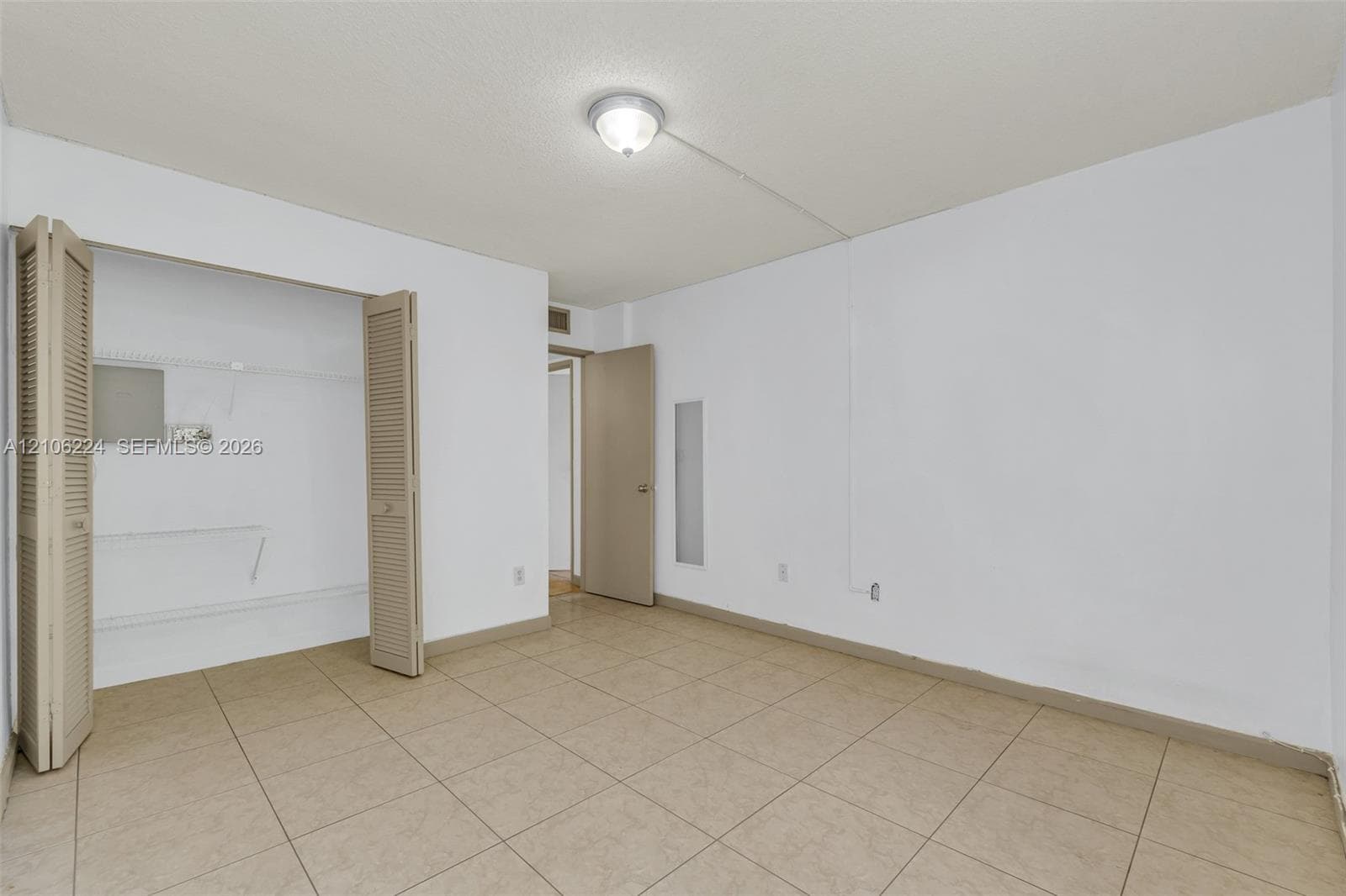 Neutral-toned tile flooring, closet with bi-fold louvered doors, and ceiling-mounted light fixture
