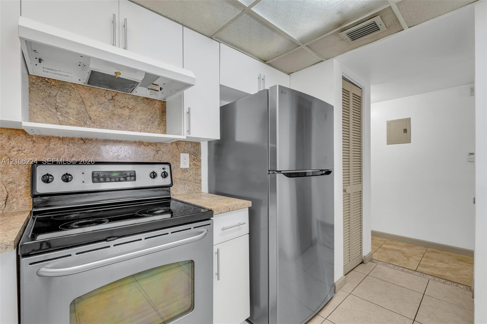 Kitchen featuring white cabinetry, stainless steel appliances, stone-finish countertops, tiled backsplash, and ceramic floor tile