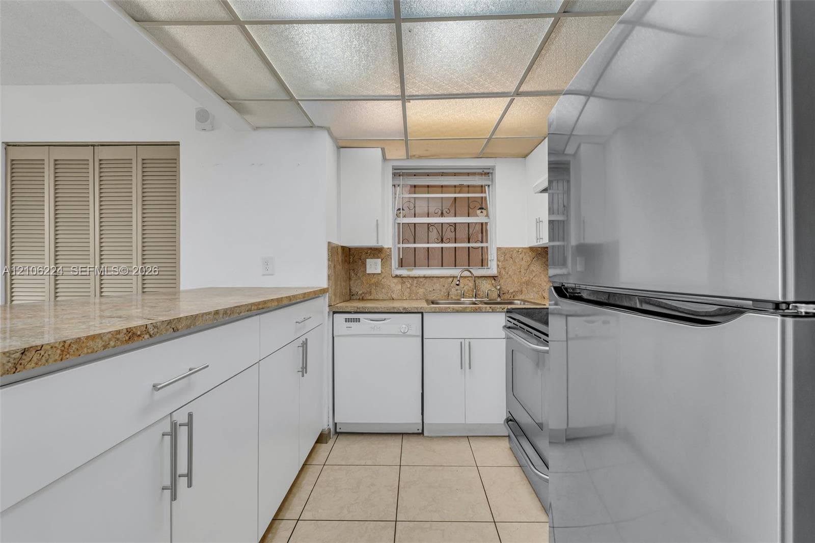 Kitchen featuring white cabinetry, stone-finish countertops, stainless steel appliances, ceramic tile flooring, and a drop ceiling